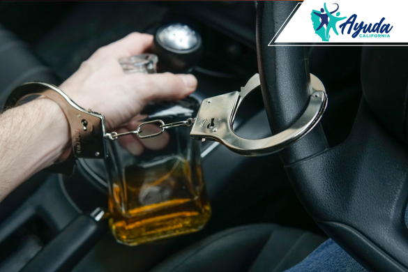 Una mano esposada sostiene una botella de alcohol mientras conduce, simbolizando las consecuencias legales y mortales de manejar bajo la influencia. La imagen refleja el reciente arresto en Fresno tras un accidente fatal por DUI, abordado por Ayuda California.