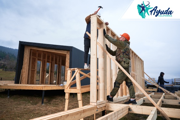 Workers raise the wooden frame of a new home after a wildfire, symbolizing the unequal recovery faced by homeowners in California amid the insurance crisis. The image reflects Ayuda California’s mission to support affected families.