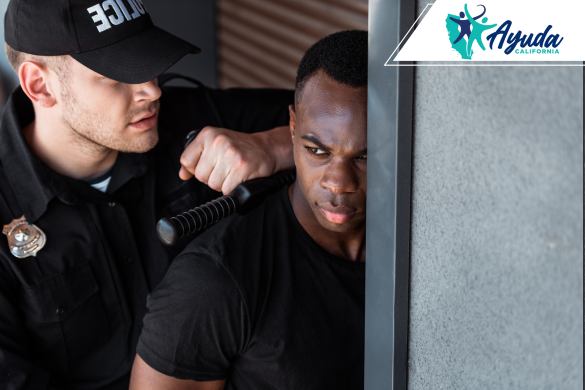 Un oficial de policía detiene a un hombre contra una pared, ilustrando preocupaciones sobre la discriminación racial y el uso indebido de la fuerza. La imagen representa el acuerdo del Departamento de Justicia con la Policía de Antioch para reformar prácticas discriminatorias y restaurar la confianza pública, como defiende Ayuda California.