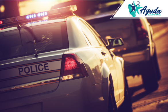 Un vehículo de policía con luces encendidas detiene a otro automóvil al atardecer, simbolizando los riesgos de las persecuciones policiales a alta velocidad. La imagen refleja el reciente caso en Fresno que dejó dos muertos y varios heridos, como reporta Ayuda California.