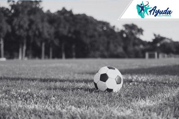 A soccer ball lies on the grass of an empty field, symbolizing the loss of innocence and pain caused by child abuse in sports settings. The image supports the report on the coach accused of abusing and murdering a minor in California, as covered by Ayuda California.